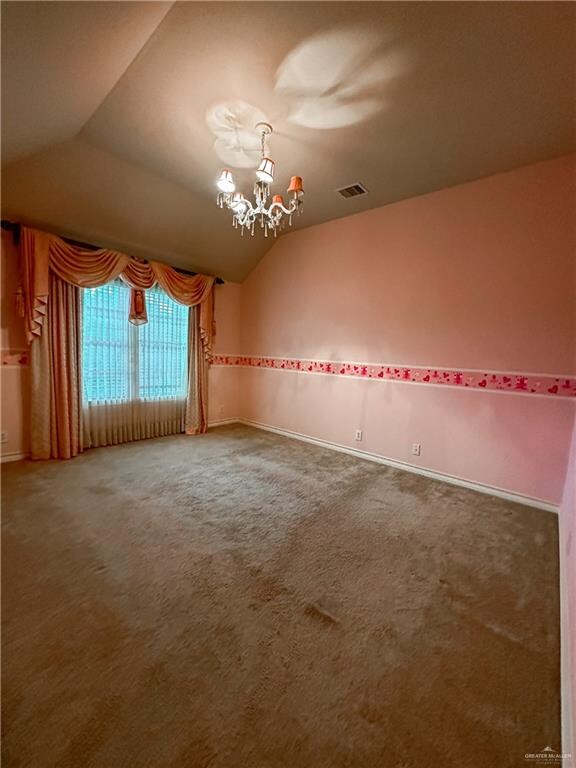 carpeted empty room featuring lofted ceiling and an inviting chandelier