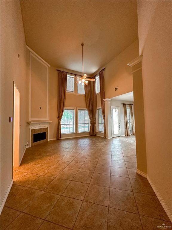 interior space with a tile fireplace, ceiling fan, light tile patterned floors, and a high ceiling