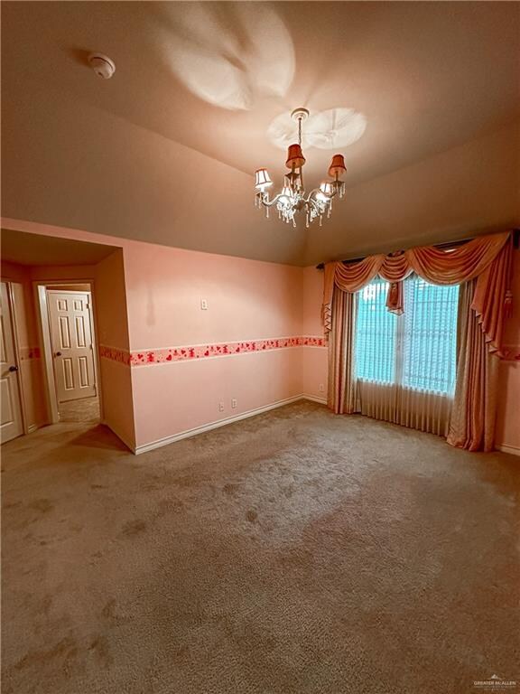 carpeted spare room featuring vaulted ceiling and a notable chandelier