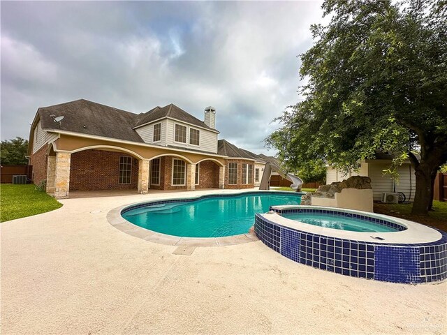 view of swimming pool with cooling unit, a patio area, an in ground hot tub, and a water slide