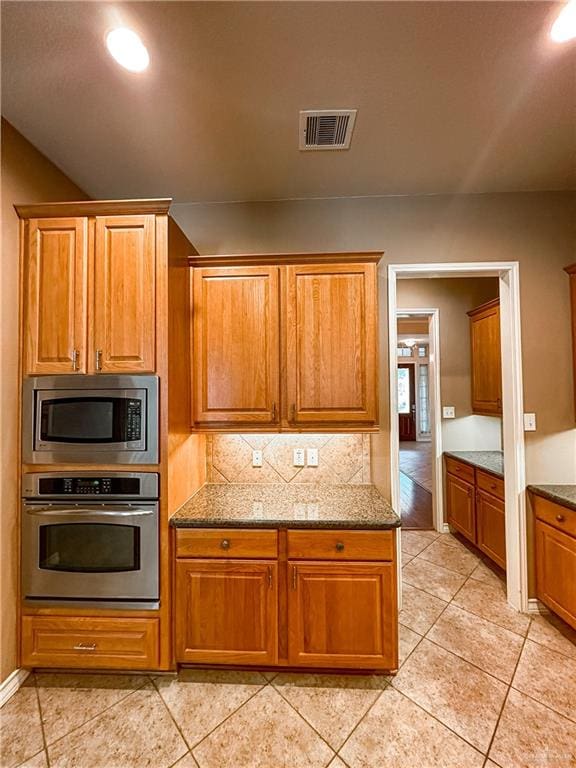 kitchen with backsplash, light tile patterned floors, stone countertops, and appliances with stainless steel finishes