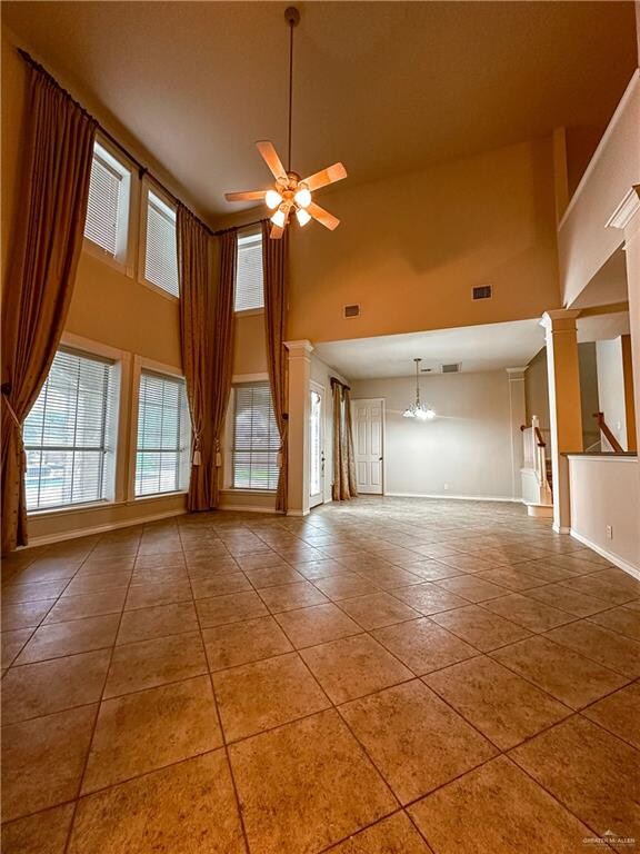 unfurnished living room featuring tile patterned flooring, ceiling fan with notable chandelier, a high ceiling, and decorative columns