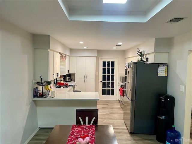 kitchen featuring white cabinetry, stainless steel fridge, kitchen peninsula, and light hardwood / wood-style flooring