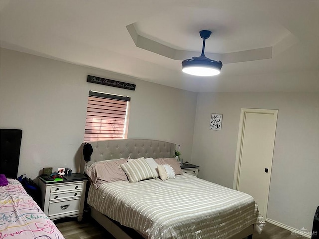 bedroom featuring ceiling fan, dark hardwood / wood-style flooring, and a tray ceiling