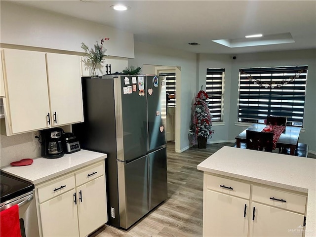 kitchen featuring white cabinets, appliances with stainless steel finishes, a raised ceiling, and light wood-type flooring