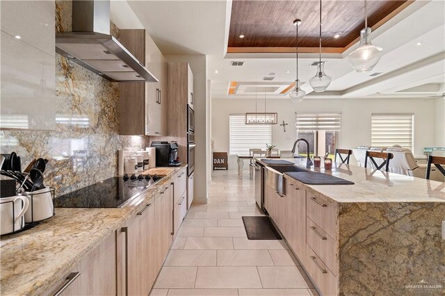 2520 Colvin Ave, Edinburg, TX 78539 - kitchen with wall chimney range hood, sink, light stone countertops, a tray ceiling, and decorative light fixtures
