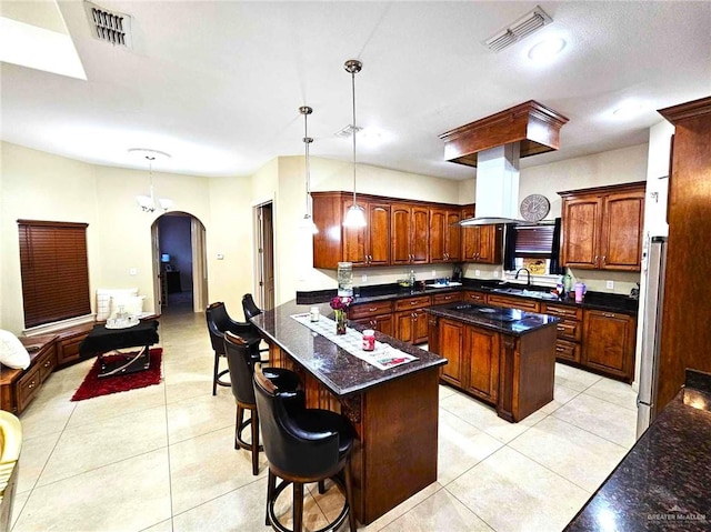 kitchen with pendant lighting, a center island, stainless steel fridge, light tile patterned floors, and island range hood