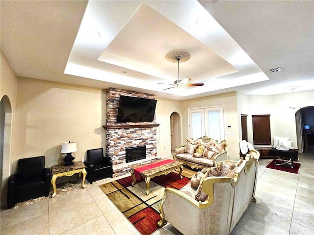 living room with ceiling fan, a stone fireplace, and a raised ceiling