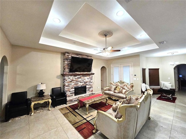 living room featuring ceiling fan, a stone fireplace, and a tray ceiling