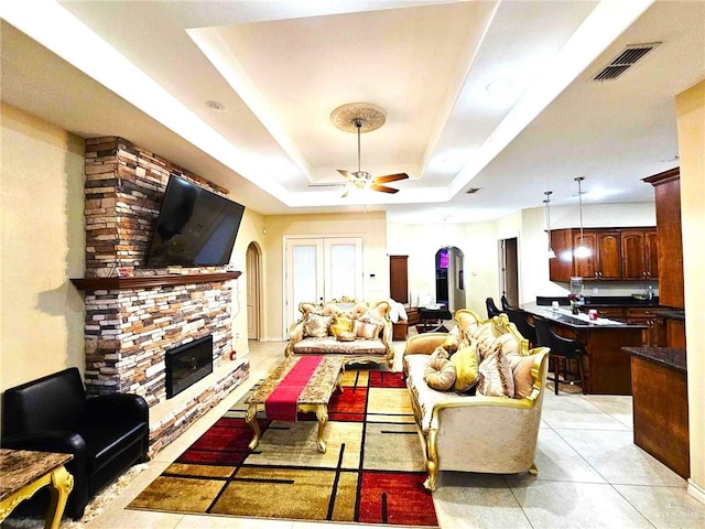 living room featuring a fireplace, a raised ceiling, and ceiling fan