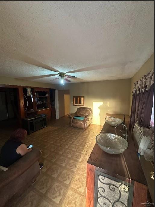 living room with a ceiling fan, light floors, and a textured ceiling