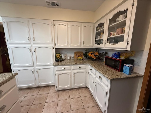 2312 Yarrow St, Mission, TX 78574 - kitchen with black microwave, white cabinets, glass insert cabinets, and light tile patterned floors