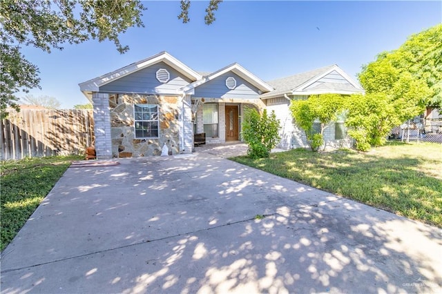 view of front facade with a front yard, concrete driveway, fence, and stone siding