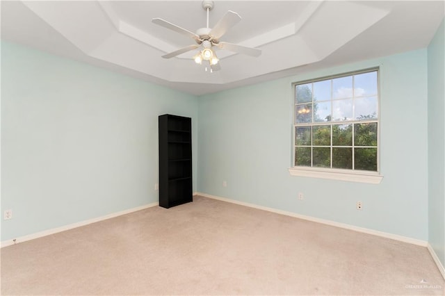 unfurnished room with ceiling fan, a raised ceiling, and light carpet