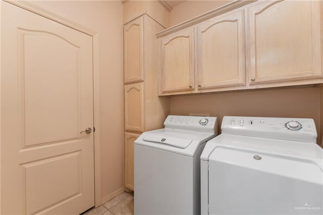 clothes washing area featuring washer and dryer, light tile patterned floors, and cabinets