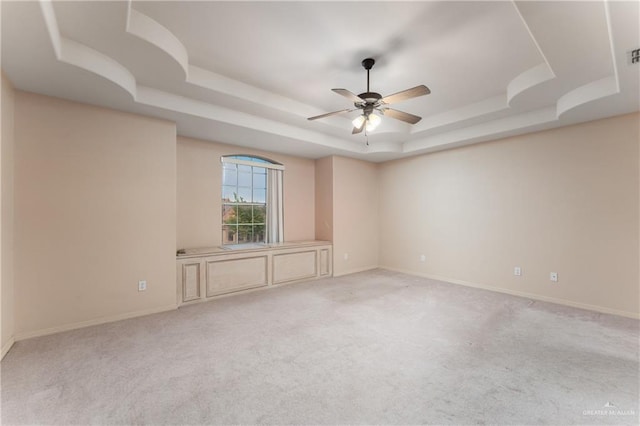 unfurnished room featuring ceiling fan, light carpet, and a tray ceiling