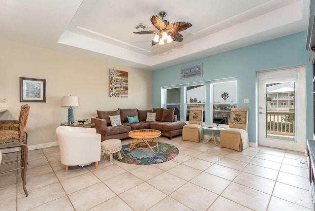 tiled living room with a tray ceiling and ceiling fan