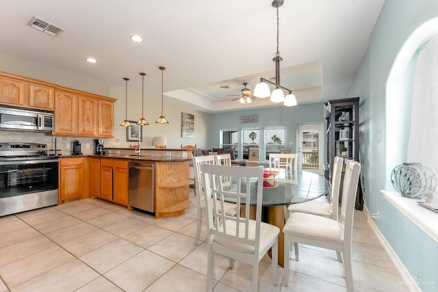 kitchen featuring ceiling fan, dark stone countertops, decorative light fixtures, a tray ceiling, and appliances with stainless steel finishes