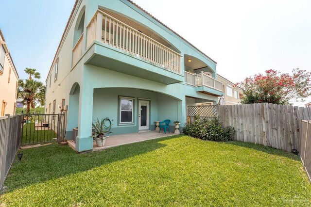 rear view of property featuring a patio area, a yard, and a balcony