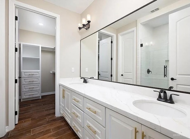 full bathroom with double vanity, a shower stall, a sink, and wood finish floors