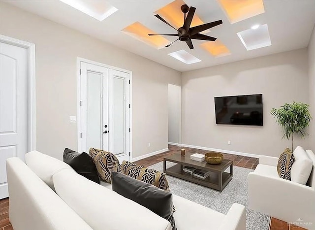 living room with ceiling fan, dark wood-type flooring, coffered ceiling, and baseboards