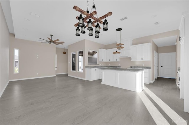 kitchen featuring a kitchen island, visible vents, baseboards, white cabinetry, and hanging light fixtures