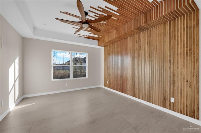 spare room with baseboards, a raised ceiling, a ceiling fan, and wooden walls