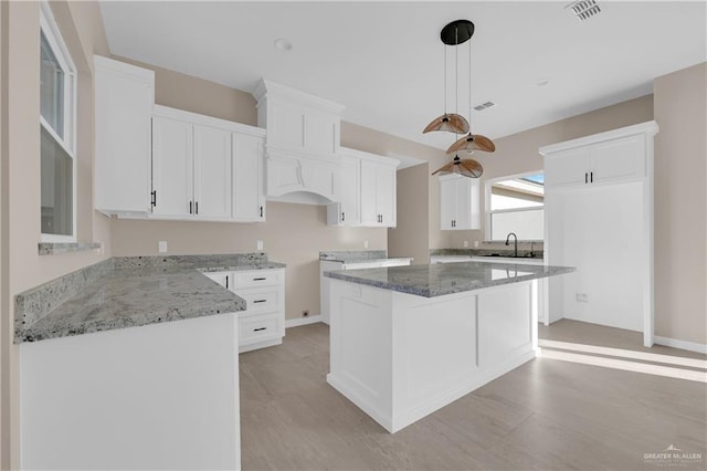 kitchen with stone countertops, a sink, visible vents, and pendant lighting