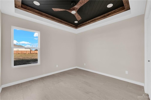 unfurnished room with wooden ceiling, ceiling fan, baseboards, and a raised ceiling