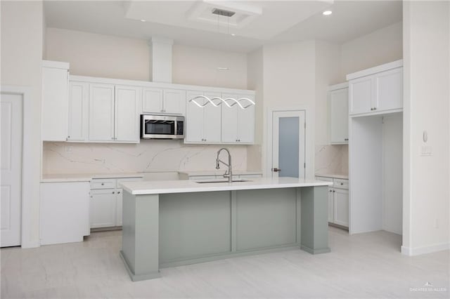 kitchen with light countertops, stainless steel microwave, a center island with sink, and a sink