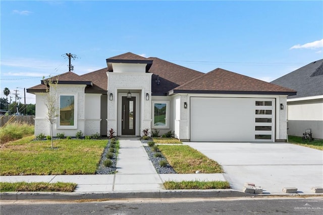 prairie-style home featuring a garage, a shingled roof, concrete driveway, a front yard, and stucco siding