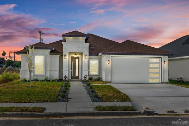 view of front facade featuring a garage, a shingled roof, concrete driveway, a yard, and stucco siding