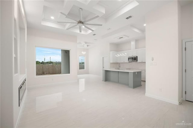 unfurnished living room with visible vents, coffered ceiling, ceiling fan, a high ceiling, and a sink