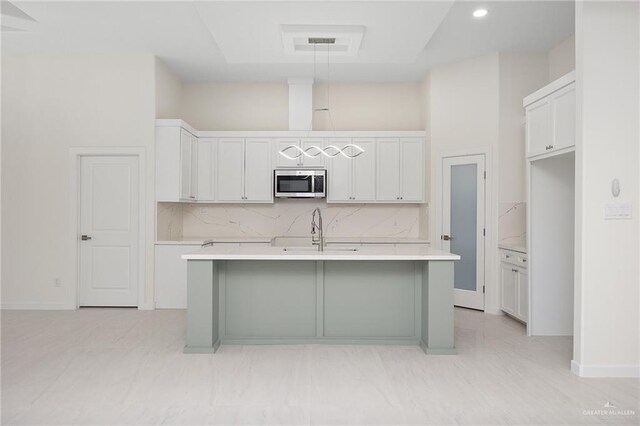 kitchen featuring stainless steel microwave, light countertops, a sink, and decorative light fixtures