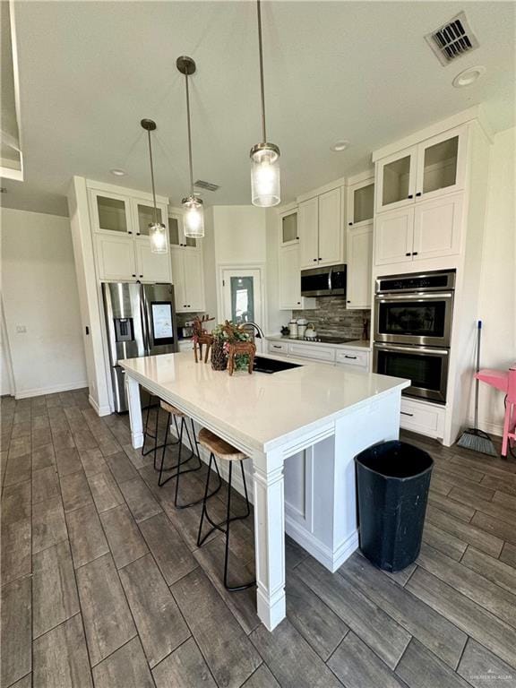 kitchen featuring sink, hanging light fixtures, an island with sink, white cabinets, and appliances with stainless steel finishes