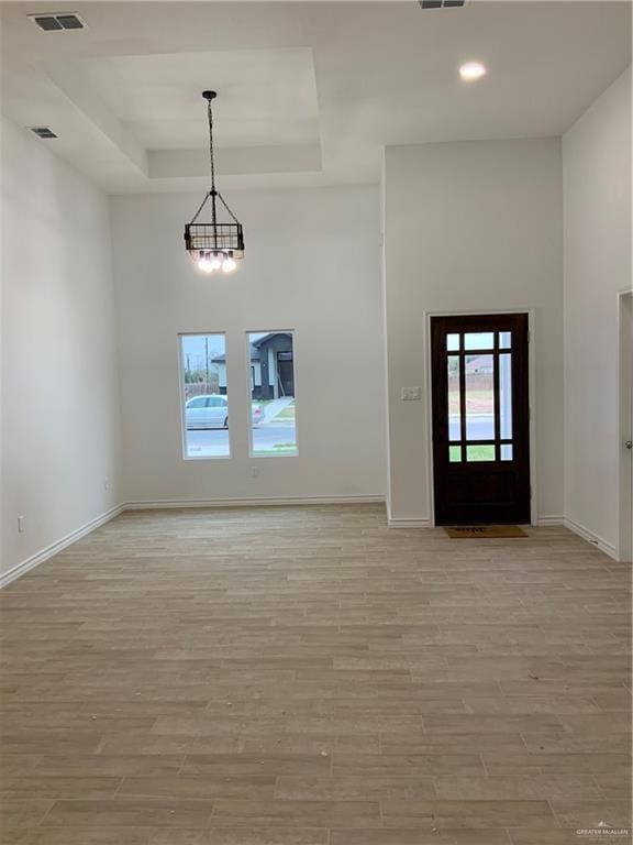 entrance foyer featuring a tray ceiling, a chandelier, and light hardwood / wood-style floors