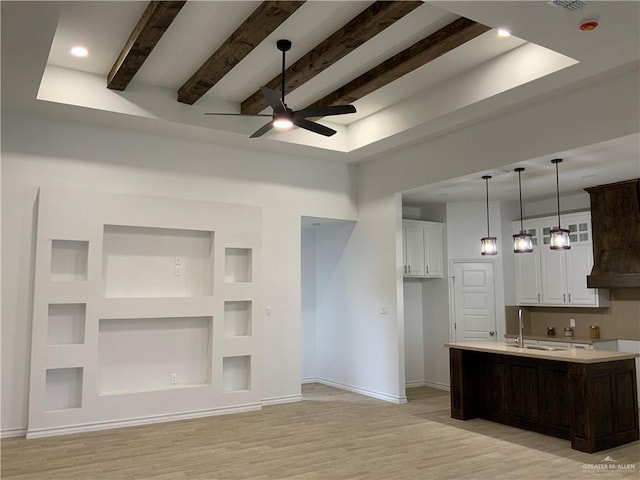 kitchen with white cabinets, a center island with sink, light wood-type flooring, beam ceiling, and dark brown cabinetry