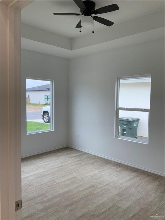 spare room featuring a raised ceiling, light hardwood / wood-style flooring, and ceiling fan