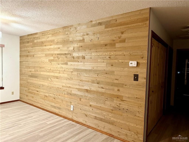 empty room featuring wooden walls, baseboards, a textured ceiling, and light wood finished floors