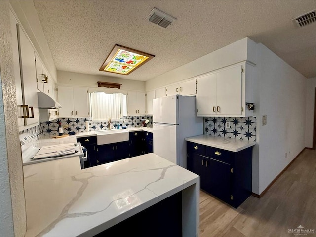 kitchen featuring stove, a sink, visible vents, white cabinets, and freestanding refrigerator