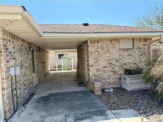 exterior space with a shingled roof, an attached carport, and brick siding