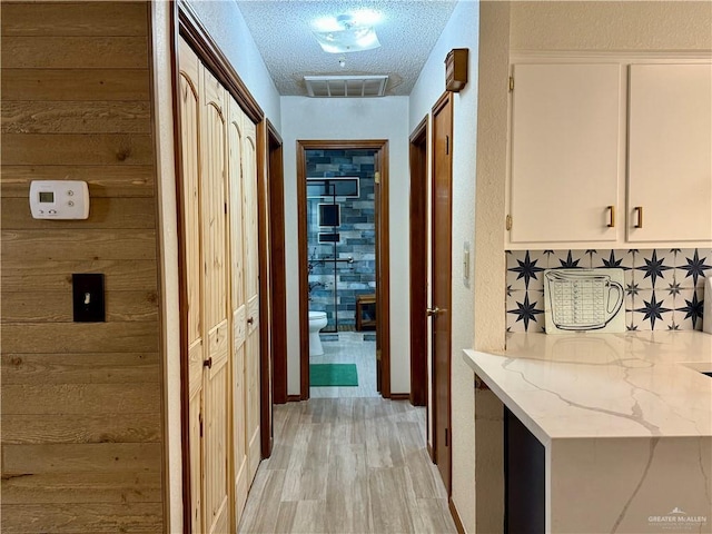 corridor featuring light wood-style flooring, visible vents, a textured ceiling, and wooden walls