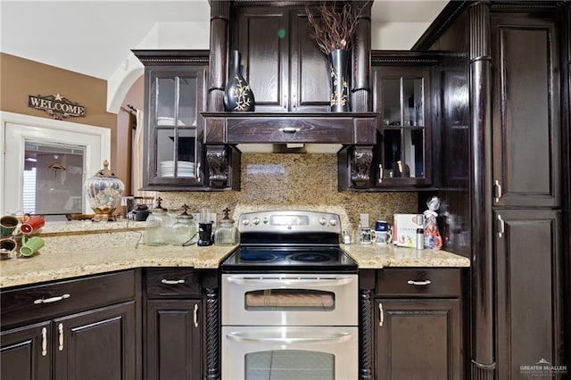 kitchen featuring double oven range, light stone counters, backsplash, and dark brown cabinetry