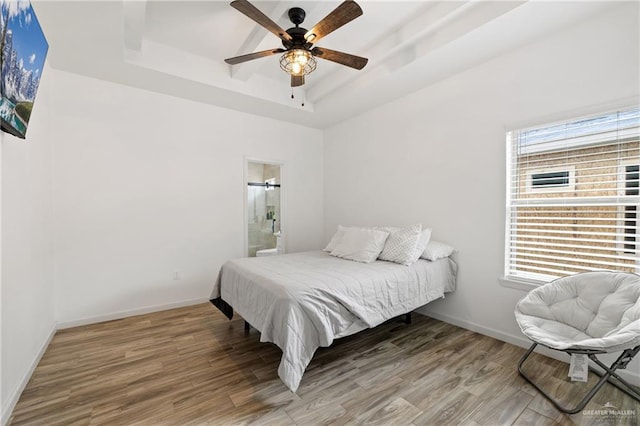 bedroom featuring hardwood / wood-style flooring, ceiling fan, ensuite bath, and a tray ceiling