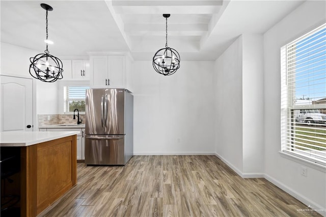 kitchen with stainless steel fridge, sink, light hardwood / wood-style flooring, white cabinetry, and hanging light fixtures