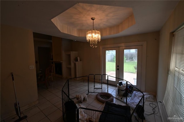 dining room with a tray ceiling, french doors, light tile patterned floors, and a chandelier