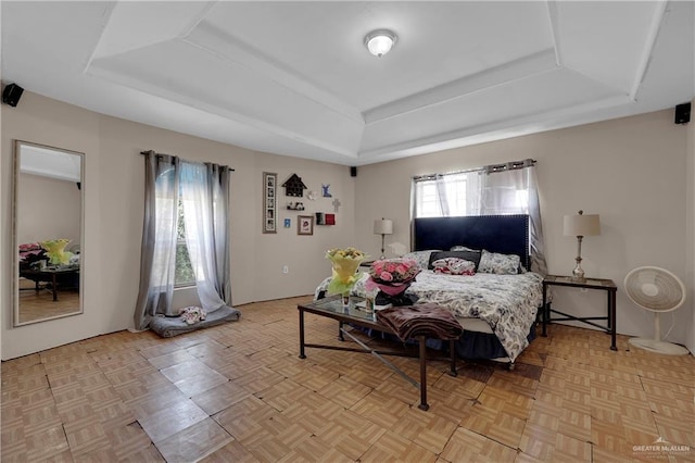 bedroom with light parquet flooring, a tray ceiling, and multiple windows