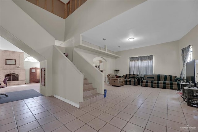 interior space with light tile patterned flooring, a towering ceiling, and a brick fireplace