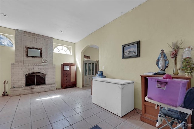 interior space featuring a high ceiling, refrigerator, a brick fireplace, and light tile patterned flooring