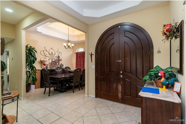 entrance foyer with a raised ceiling, light tile patterned floors, a chandelier, and baseboards